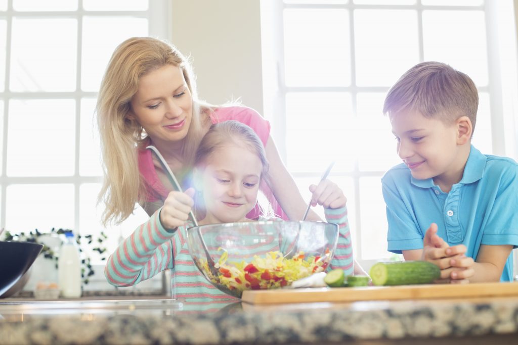 Family looking at girl mixing salad in kitchen