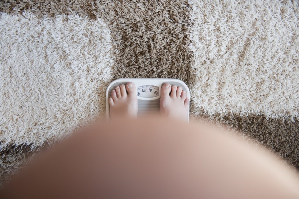 Pregnant woman weighing herself on a bathroom scale. View from above. No face. Focus on weight scale . Self portret